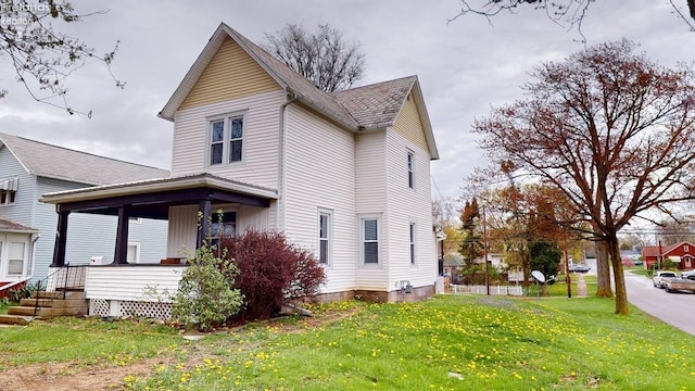 view of side of property featuring a lawn, a porch, and a shingled roof