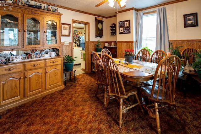 113 W Grant St, Clyde, OH 43410 - dining space featuring wainscoting, dark colored carpet, ornamental molding, wood walls, and ceiling fan