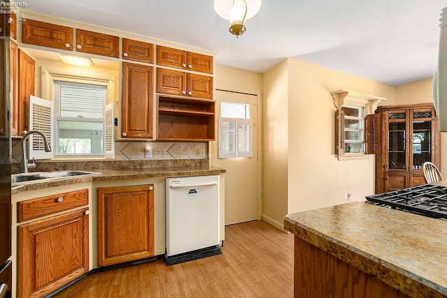 kitchen with a sink, light wood-style floors, backsplash, and white dishwasher