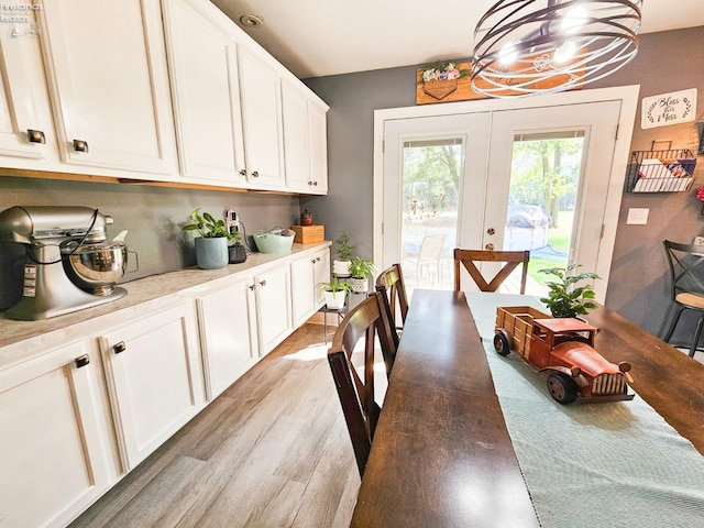 dining space featuring light wood-type flooring, french doors, and a notable chandelier