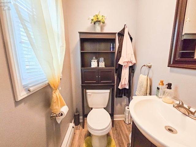 half bathroom featuring a baseboard heating unit, a sink, toilet, baseboards, and wood finished floors
