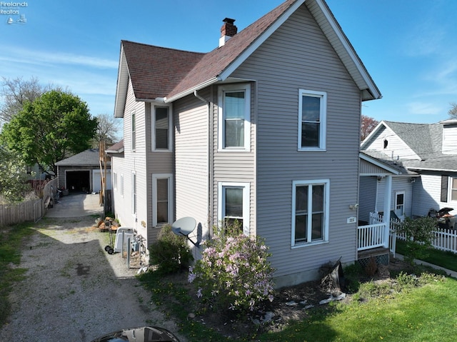rear view of house featuring fence, an outdoor structure, a chimney, and roof with shingles