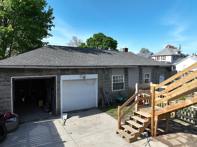 rear view of house featuring a garage, a chimney, driveway, and roof with shingles
