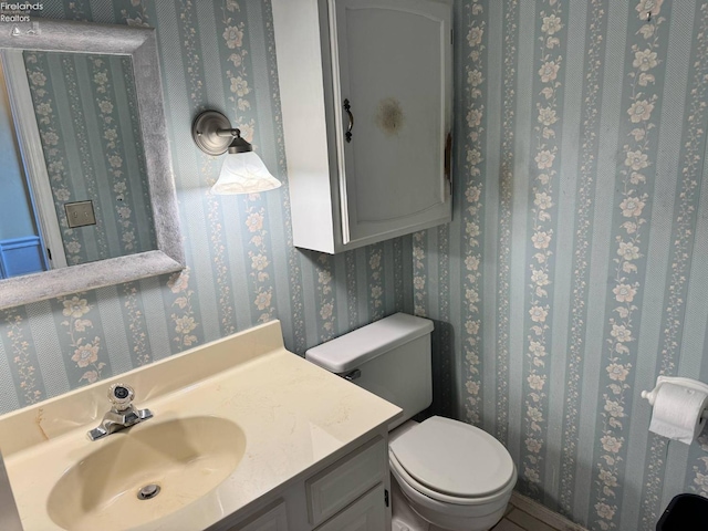 half bath with vanity, toilet, and wallpapered walls