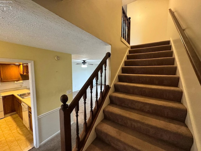 staircase featuring a textured ceiling, ceiling fan, and baseboards
