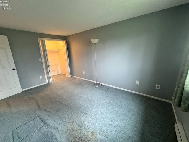 unfurnished bedroom featuring a walk in closet, carpet flooring, baseboard heating, and baseboards