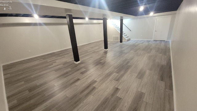 finished below grade area featuring visible vents, stairway, wood finished floors, and baseboards