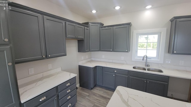 kitchen with recessed lighting, light stone countertops, a sink, and light wood-style flooring
