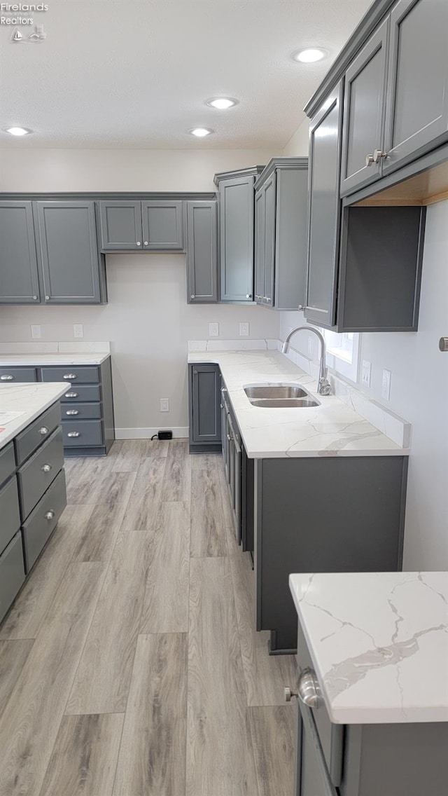 kitchen with recessed lighting, light stone countertops, a sink, light wood-type flooring, and gray cabinetry