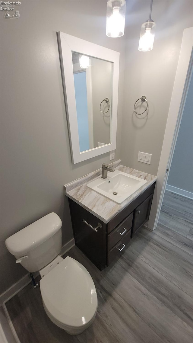 half bathroom with baseboards, wood finished floors, toilet, and vanity