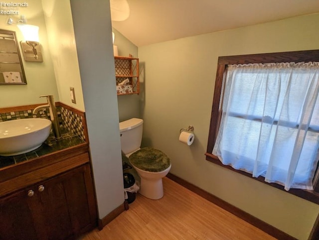bathroom featuring vanity, toilet, baseboards, wood finished floors, and vaulted ceiling