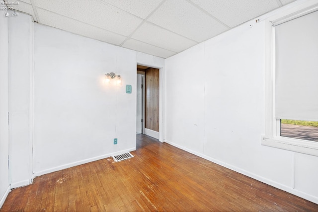 unfurnished room featuring baseboards, visible vents, a drop ceiling, and hardwood / wood-style flooring