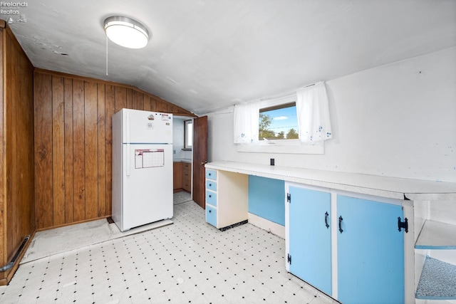kitchen featuring light countertops, freestanding refrigerator, lofted ceiling, light floors, and blue cabinets