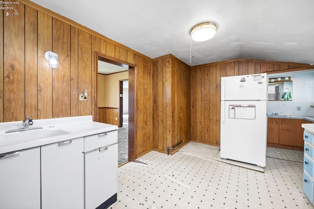 kitchen featuring freestanding refrigerator, wooden walls, a sink, and light countertops