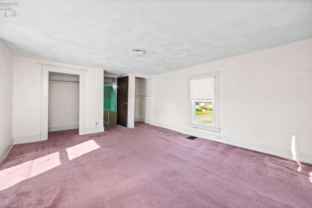 unfurnished bedroom featuring baseboards, carpet floors, and two closets