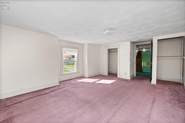 unfurnished bedroom with baseboards, light carpet, and multiple closets