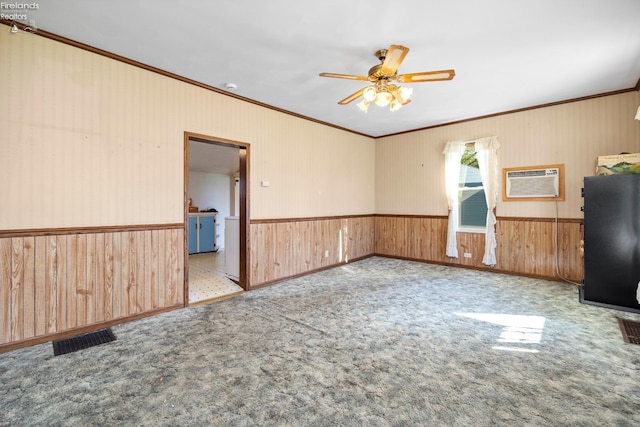 empty room with crown molding, wood walls, visible vents, ceiling fan, and a wainscoted wall