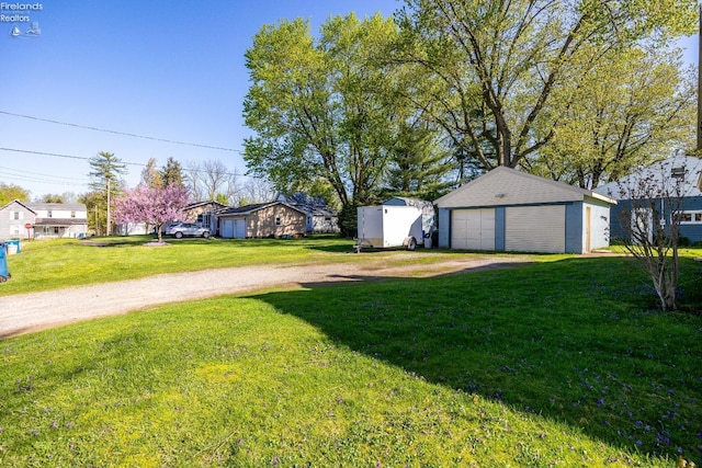 view of yard with a detached garage, driveway, and an outdoor structure