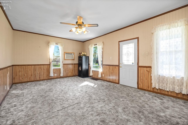 unfurnished room featuring wooden walls, wainscoting, carpet floors, a ceiling fan, and ornamental molding