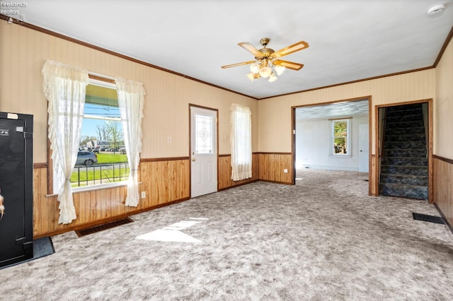 unfurnished room featuring crown molding, wooden walls, wainscoting, and a wealth of natural light