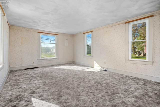 carpeted spare room featuring plenty of natural light, wallpapered walls, and visible vents