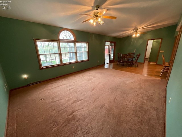 unfurnished living room with carpet, baseboards, a ceiling fan, and visible vents
