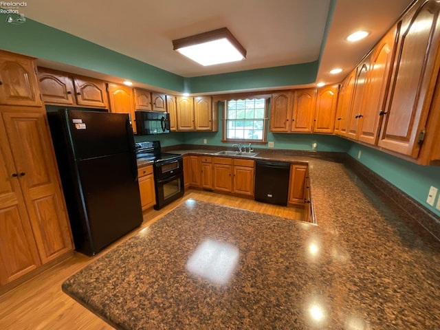 kitchen with a sink, a peninsula, brown cabinetry, and black appliances