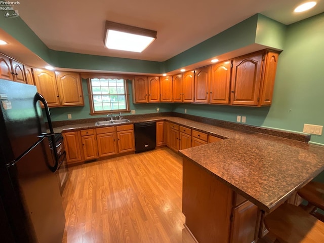 kitchen featuring a sink, a peninsula, black appliances, and dark countertops