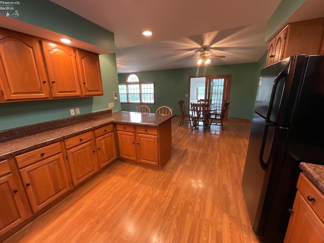kitchen with dark countertops, freestanding refrigerator, a peninsula, and light wood-type flooring