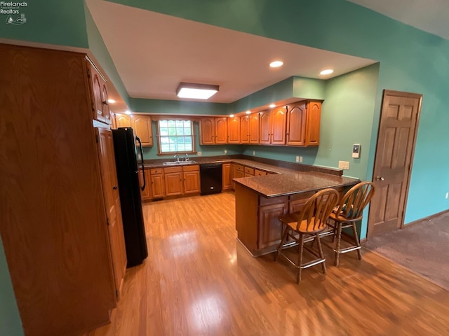 kitchen with a sink, a peninsula, black appliances, dark countertops, and light wood-type flooring