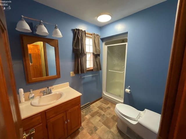 bathroom with toilet, vanity, a shower stall, stone finish flooring, and baseboards