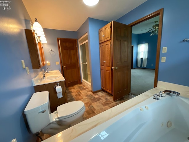 bathroom with toilet, a tub with jets, a ceiling fan, stone finish flooring, and baseboards