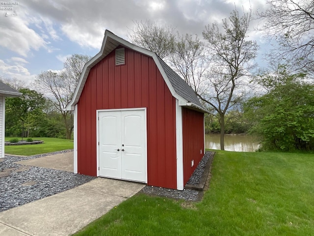 view of barn with a storage shed, a water view, and a lawn