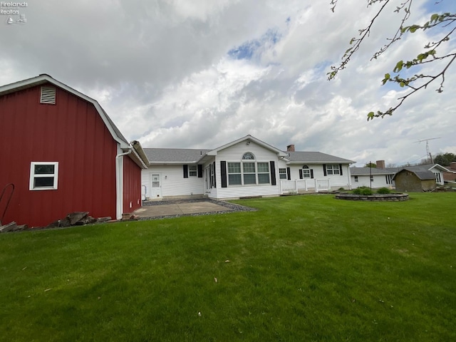 rear view of property featuring a patio, a barn, a chimney, a lawn, and an outdoor structure