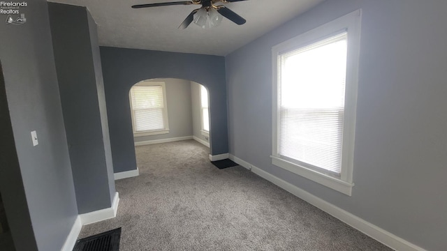 spare room featuring carpet floors, arched walkways, ceiling fan, and baseboards