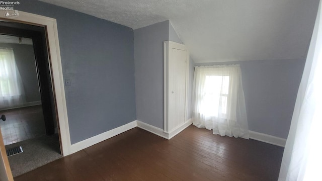 unfurnished room with visible vents, dark wood-style flooring, baseboards, a textured ceiling, and vaulted ceiling