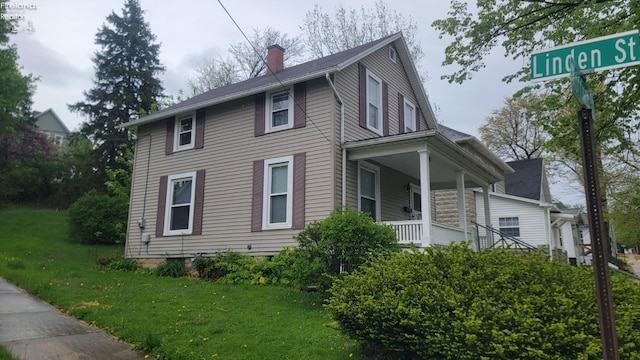 view of side of property with a yard, a chimney, and covered porch