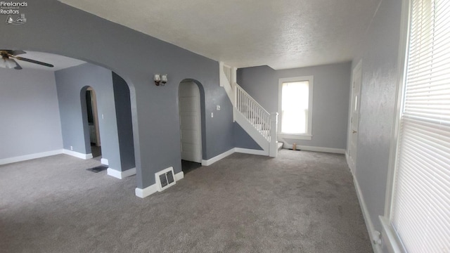 unfurnished living room with carpet flooring, arched walkways, ceiling fan, and stairs