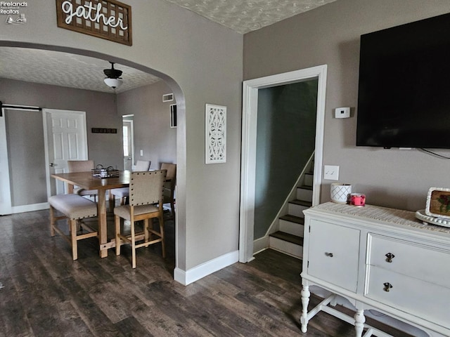dining area featuring arched walkways, baseboards, dark wood finished floors, and a textured ceiling