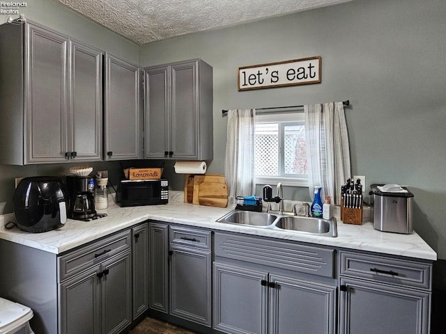kitchen with a textured ceiling, gray cabinets, black microwave, and a sink