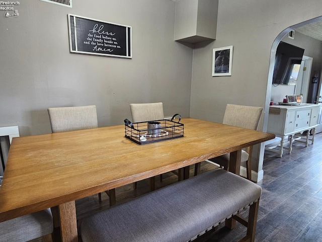 dining room featuring arched walkways, visible vents, and dark wood-style floors
