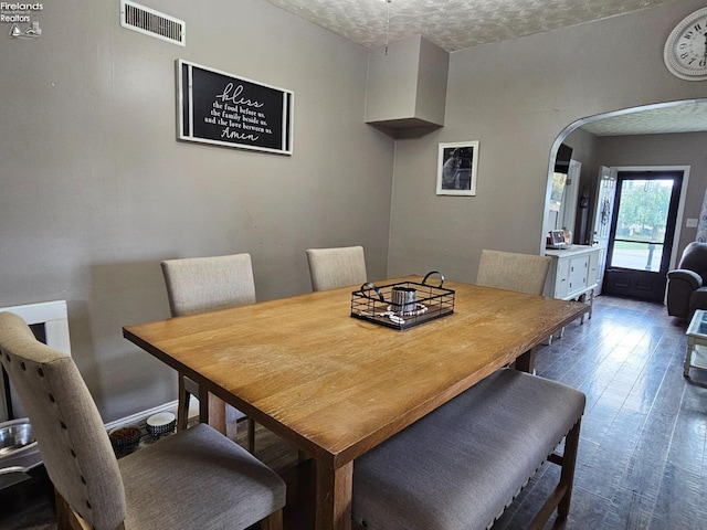 dining area featuring visible vents, arched walkways, and dark wood-style floors
