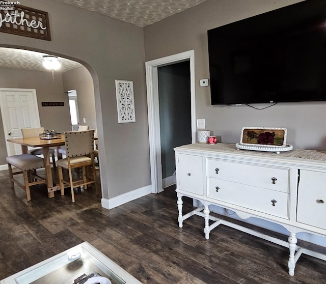 interior space featuring baseboards, arched walkways, dark wood finished floors, and a textured ceiling