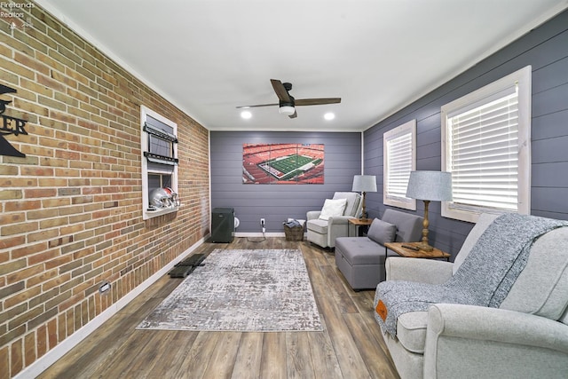 living area with crown molding, brick wall, a ceiling fan, recessed lighting, and wood finished floors