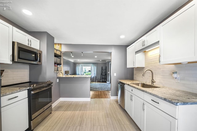 kitchen featuring decorative backsplash, appliances with stainless steel finishes, a sink, baseboards, and white cabinets