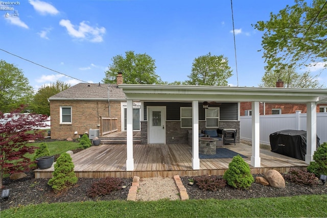 rear view of property with fence, an outdoor fire pit, brick siding, a deck, and a chimney