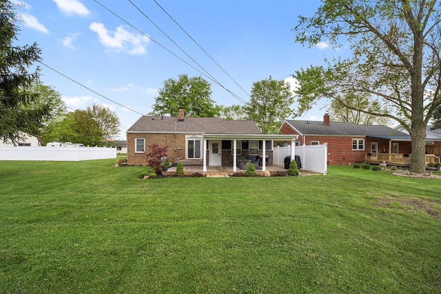 back of house featuring a lawn, a chimney, fence, and brick siding