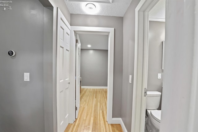 corridor featuring baseboards, light wood finished floors, and a textured ceiling