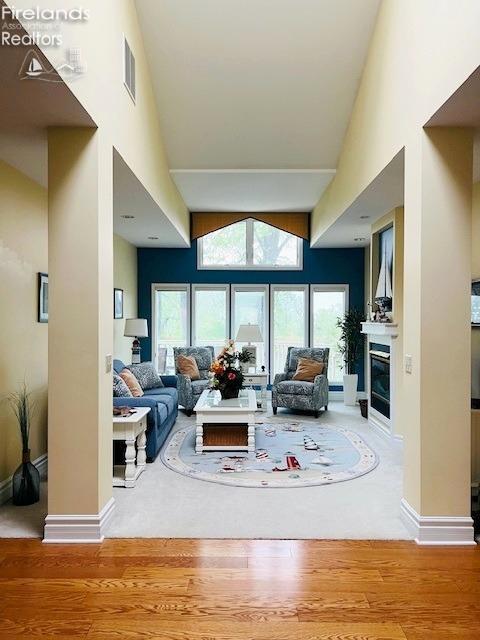 living area featuring baseboards, a high ceiling, a glass covered fireplace, and wood finished floors