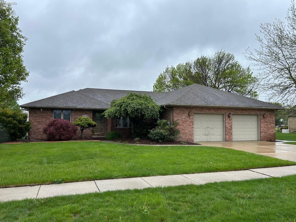 ranch-style home featuring a garage, concrete driveway, a front lawn, and brick siding